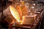 Two workers pouring molten metal from flask in foundry