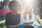 Two young female friends on park bench looking at digital tablet, Como, Italy