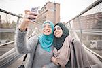 Two female friends on footbridge taking smartphone selfie