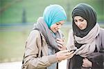 Two young women at lakeside texting on smartphone