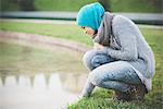 Young woman wearing hijab crouching at park lakeside