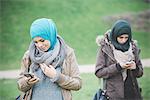 Two female friends in park reading texts on smartphones