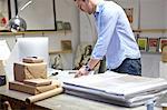 Man wrapping frames in bubble wrap on table in picture framers workshop