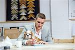 Mid adult man with dog at making notes at desk in picture framers workshop