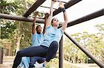 Determined woman swinging on monkey bars on boot camp obstacle course