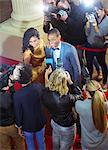 Celebrity couple being interviewed and photographed by paparazzi at red carpet event