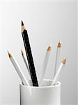 Tall black pencil in cup with smaller white pencils still life