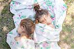 Twin girls napping in floral sheet on grass