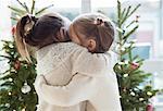 Girls hugging in front of Christmas trees