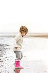 Girl in pink rain boots playing in water on beach