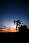 A pumpjack at an oil drilling site at sunset.