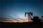 A pumpjack at an oil drilling site at sunset.