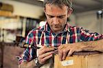 An antique furniture restorer working with his hands using a sharp tool on the edge of a piece of wooden furniture.