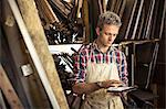 An antique furniture restorer in his workshop, using a digital tablet.