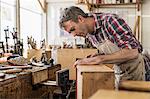 An antique furniture restorer in his workshop using a hand tool to smooth a wooden object.