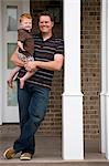 father standing on front porch holding baby son