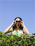 woman looking over a hedge with binoculars