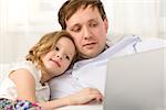 Father and little daughter on the sofa at home. Father holding laptop,  girl using it leaning on dads shoulder