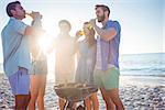 Happy friends doing barbecue and drinking beer at the beach