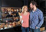 Couple in bakery buys fresh bread, shop assistant in background