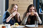 Two young women eating sandwiches in a cafe