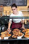 Waitress arranging cake at display cabinet in coffee shop