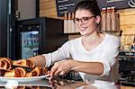 Waitress in coffee shop arranging croissants on counter