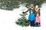 Family with two children stands with Christmas tree in snow-covered landscape, Bavaria, Germany