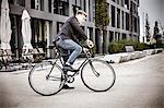 Young businessman riding bicycle on city street, Munich, Bavaria, Germany