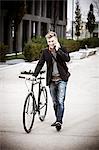 Young businessman with bicycle using phone, Munich, Bavaria, Germany