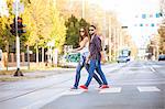 Young couple with skateboard crossing city street