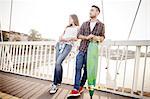 Young couple with skateboard waiting on bridge