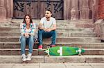 Young couple with skateboard taking a break on staircase