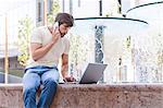 Male university student using mobile phone and laptop