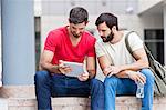 Two male university students using digital tablet on campus