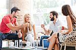 Male students in cafe preparing for fist bump, girlfriends watching