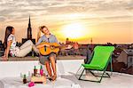 Young woman with girlfriend at rooftop party playing guitar
