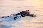 Little boy lying on back in snow