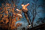 Male runner jumping over bench in park