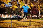 Male runner jumping over fence in autumn park