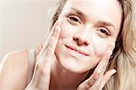 Young woman applying lotion on face, close-up