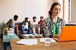 Creative businesswoman working at laptop with paperwork in office