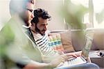 Casual businessmen working at laptop on sofa in office