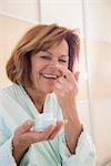 Senior woman applying moisturizer on her face, Munich, Bavaria, Germany