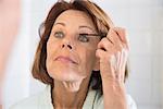 Senior woman applying eye make up with mascara, Munich, Bavaria, Germany