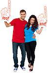 Excite young couple showing boo hurray foam hand and cheering against white background