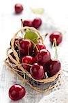 Ripe cherries in small basket. On white wooden table.