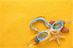 Blue glasses for swim and seashells on yellow sand.