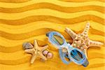 Blue swimming goggles, pebbles and seashells on yellow sand.