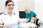 Smiling dentist, assistant examining a patient behind